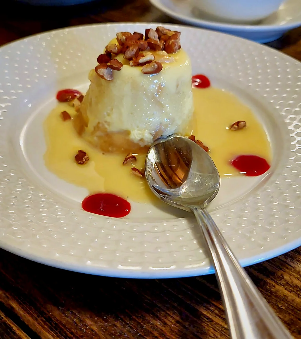 A plated vanilla custard dessert with toasted pecans and berry sauce